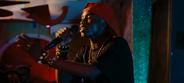 Image du film Congo Boy de Rafiki Fariala : un jeune homme en casquette rouge chante au micro sur une scène